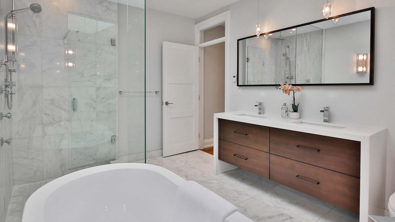 A clean modern bathroom with a marble-tiled walk-in shower, a freestanding tub and a double vanity under a long mirror