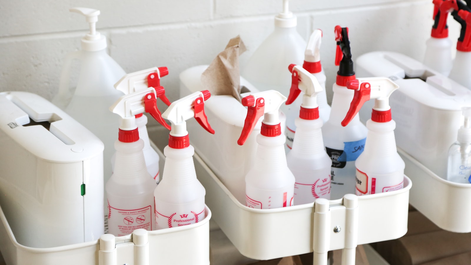 A row of white spray bottles with red trigger nozzles standing upright in a white caddy