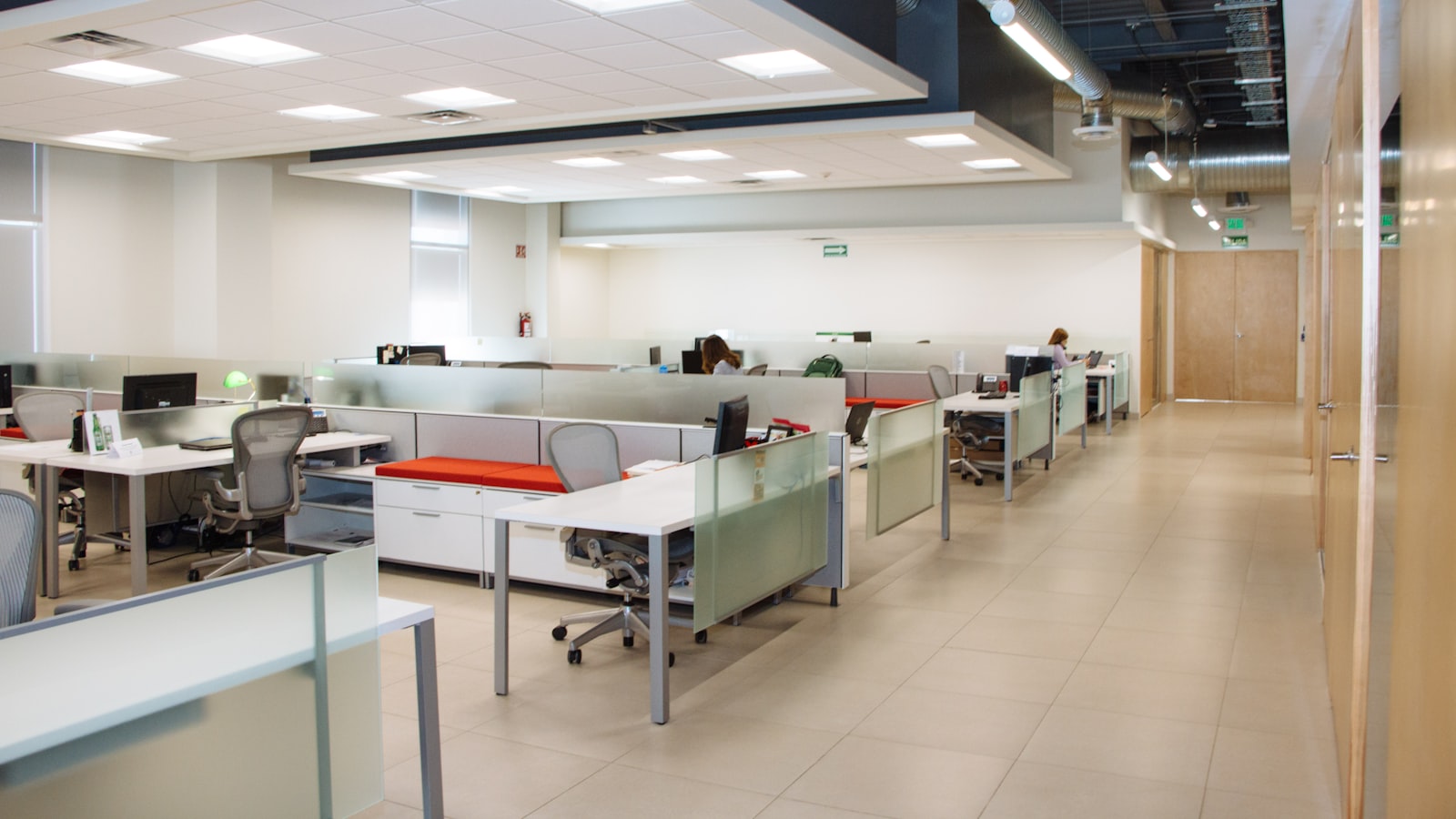 An empty open-plan office after hours, with rows of white desks, task chairs and glass partitions under ceiling lighting